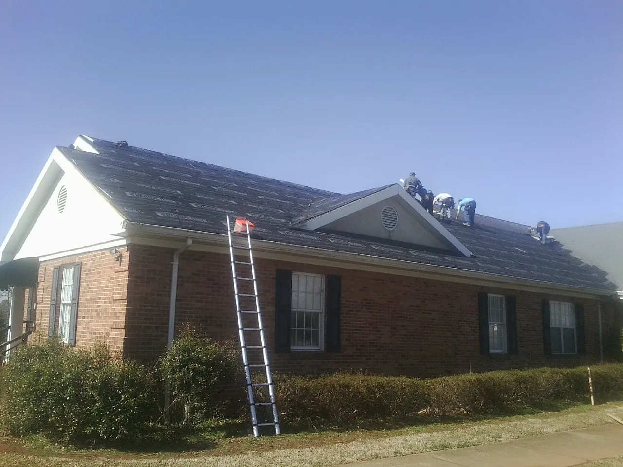 Crew tearing shingles off a brick ranch roof with a ladder set — Emergency Roof Repair work by our crew in Argyle
